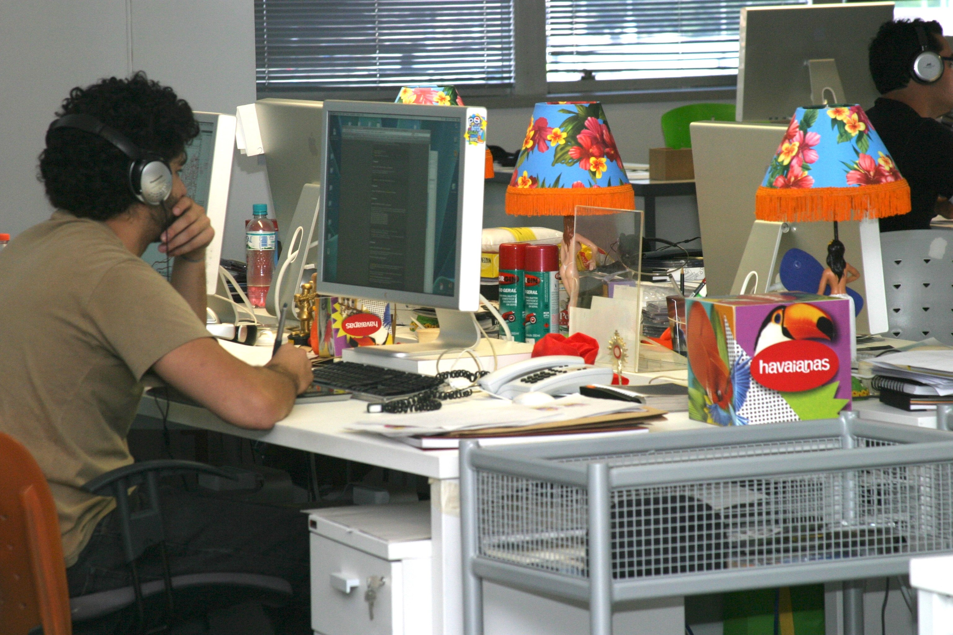 An art director at his desk at AlmapBBDO in São Paulo, flanked by Havaianas-branded desk accessories and floral lampshades.