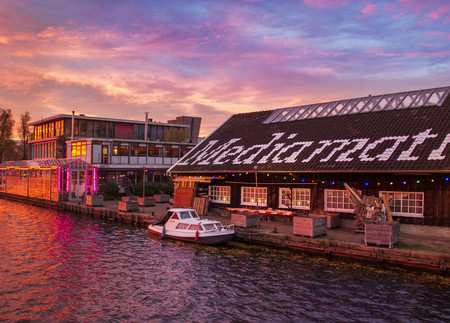 Mediamatic's waterside building in Amsterdam lit up at sunset, with a boat moored alongside.