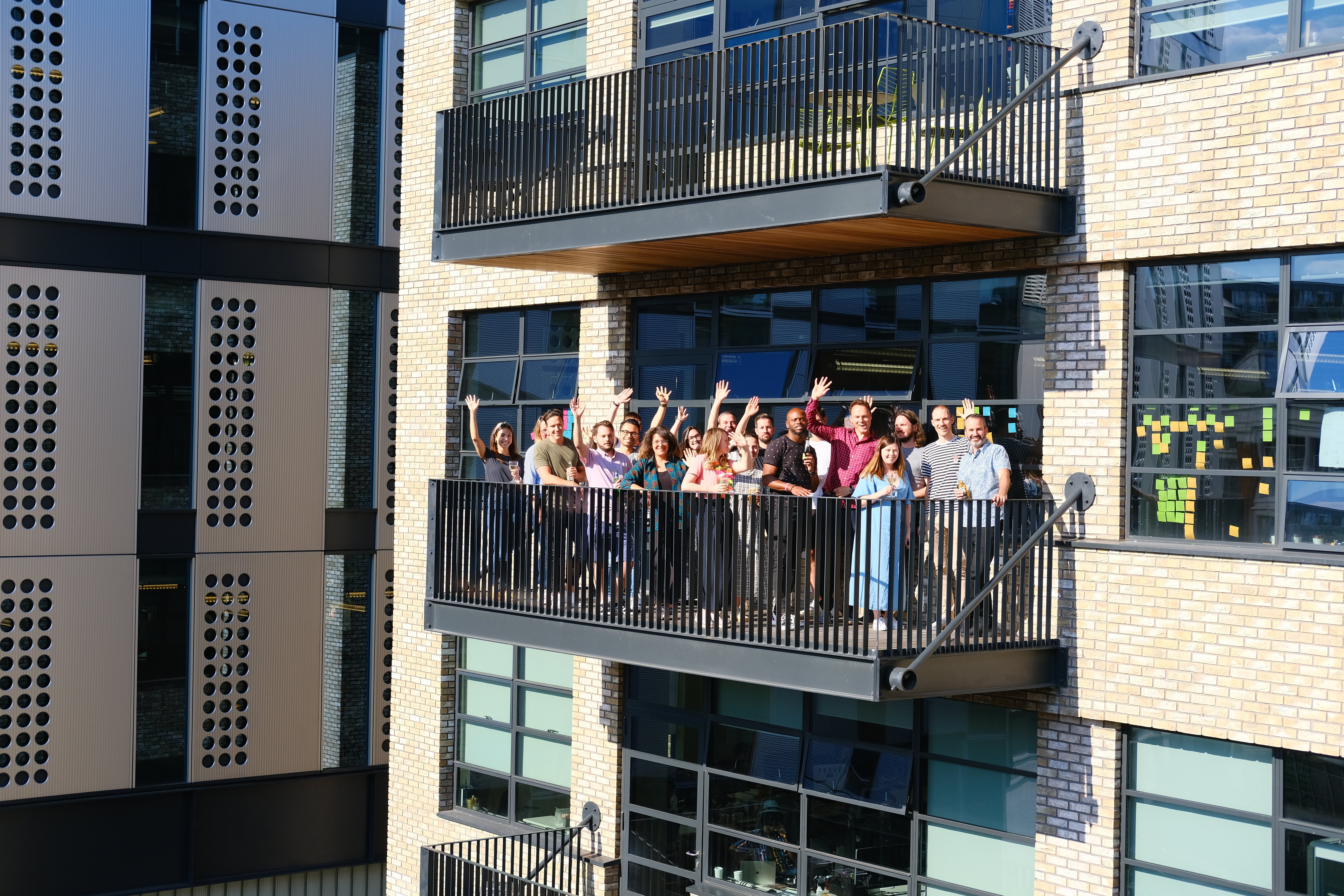 The whole Red Badger team waving from a building balcony, celebrating with drinks in hand.