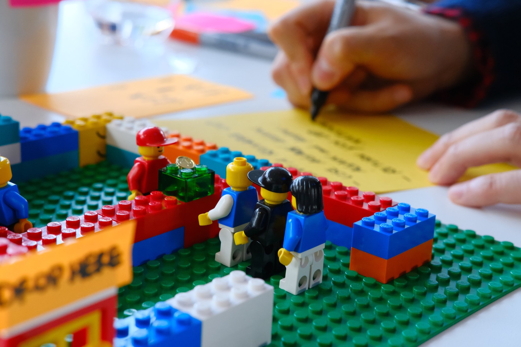 A cross-functional team using LEGO Serious Play to model in-person service, with a participant capturing notes on a sticky