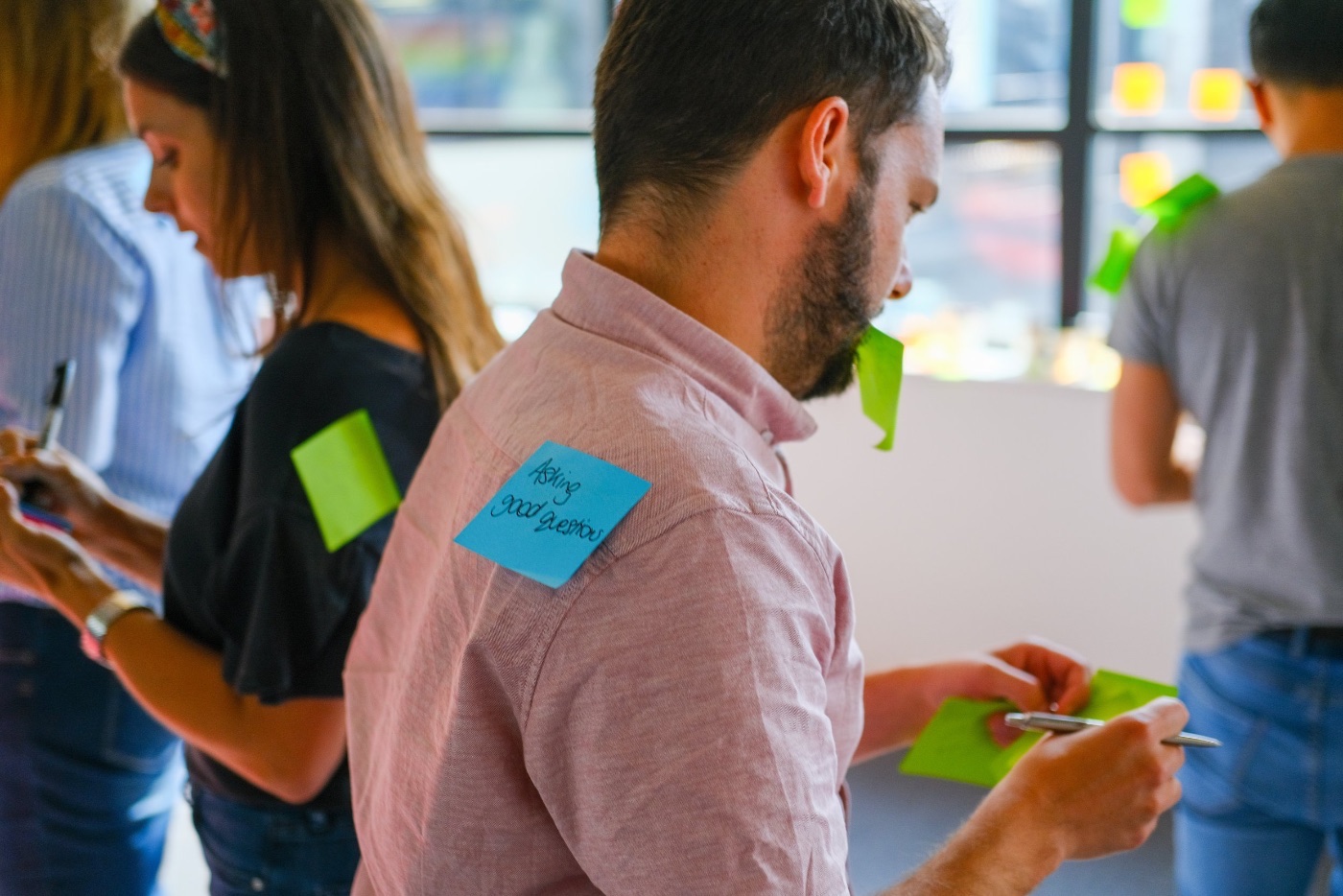 A workshop participant with an Asking good questions sticky note on their shoulder, surrounded by colleagues sketching ideas