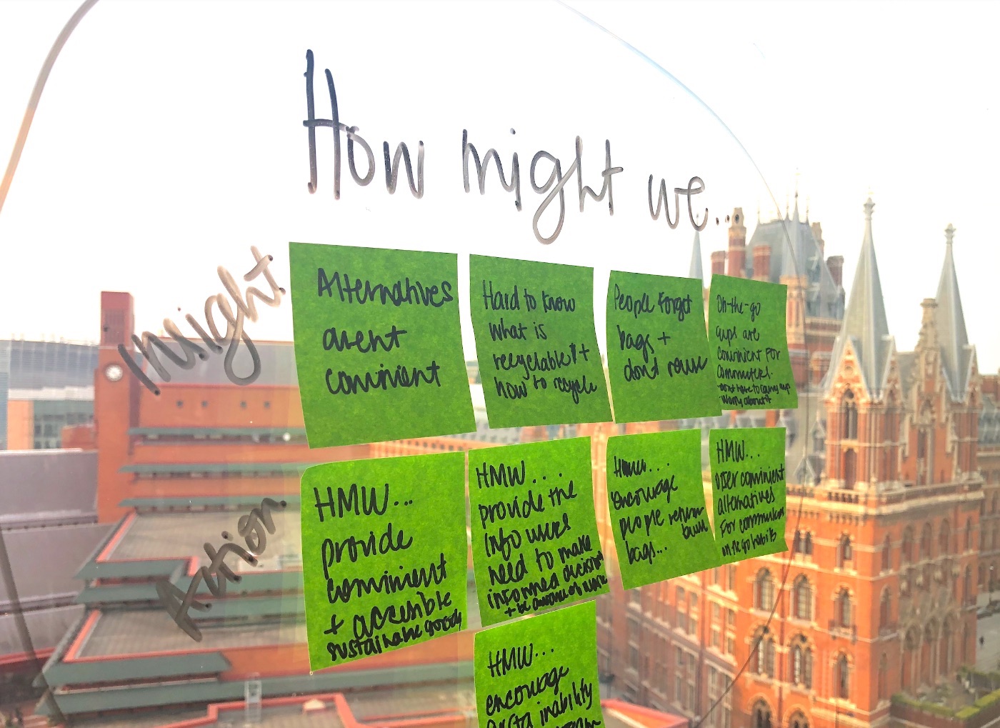 A glass wall of green How Might We sticky notes from a design workshop