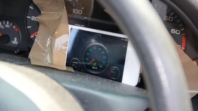 A smartphone running a speedometer app, taped into a car dashboard next to the built-in speedometer, as an improvised replacement.