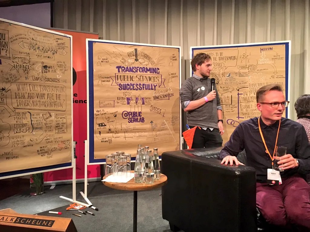 Panel discussion in front of large graphic-recording posters titled &lsquo;Transforming Public Services Successfully.&rsquo;